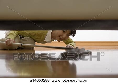 Stock Photo - Mid Adult Woman mopping under the sofa. Fotosearch