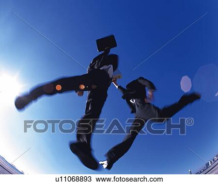 Stock Image - Two Businessmen Jumping, Low Angle View, Lens Flare, Long Exposure. Fotosearch