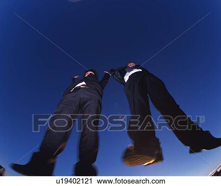 Stock Image - Two Businessmen Jumping, Low Angle View, Lens Flare, Long Exposure, Copy Space. Fotosearch