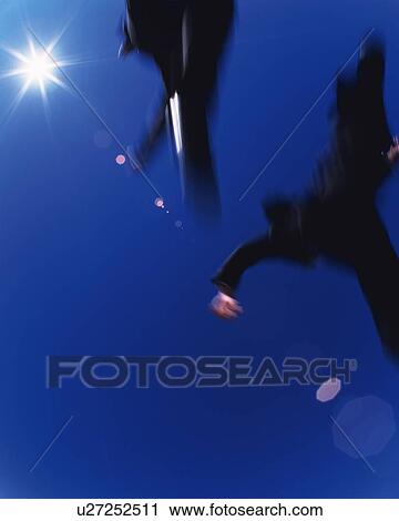 Stock Image - Two Businessmen Jumping, Low Angle View, Lens Flare, Long Exposure, Copy Space. Fotosearch