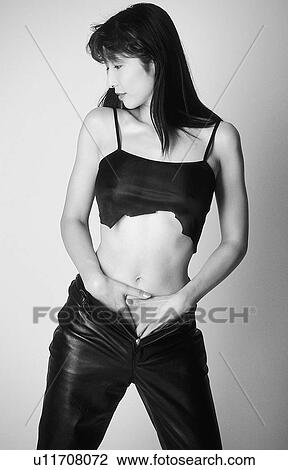 Stock Image - Portrait of a woman standing in tore top and leather pants, black and white, front view, white background. Fotosearch