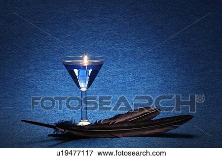 Stock Photo - Light in Cocktail Glass and Two Feathers, Copy Space. Fotosearch