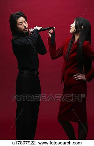 Stock Image - Woman in Red Pulling a Tie of Man in Black, Side View. Fotosearch
