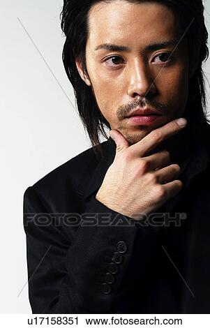 Stock Image - Young Man in Black Holding Chin, Front View. Fotosearch
