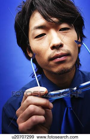 Stock Photo - Young Man in Blue Taking Off His Glasses, Front View. Fotosearch