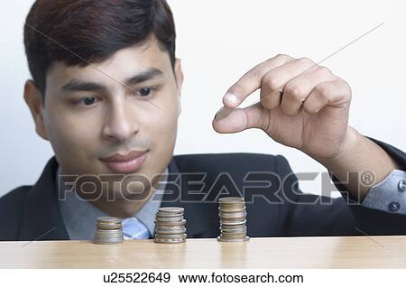 Stock Photo - Close-up of a businessman putting a coin on a stack of coins. Fotosearch