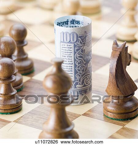 Stock Photograph - Close-up of a rolled up Indian one hundred rupee banknote on a chessboard with chess pieces. Fotosearch
