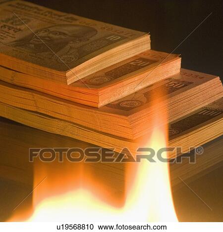 Stock Image - High angle view of a stack of Indian banknotes of different denominations near a flame. Fotosearch