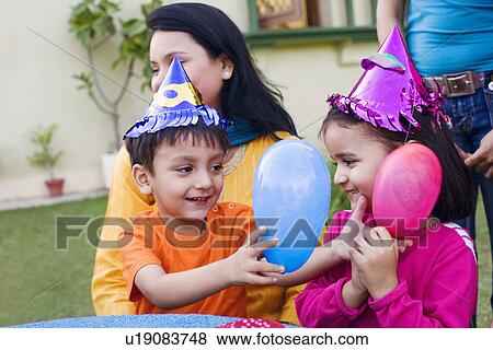 Stock Photo - Boy and a girl playing with balloons and their mother sitting beside them. Fotosearch