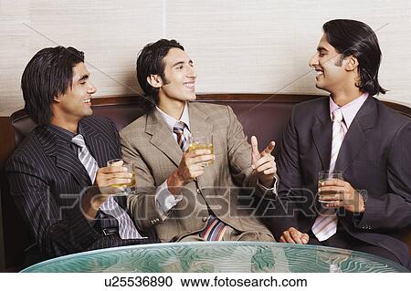 Stock Image - Close-up of three businessmen holding glasses of whiskey. Fotosearch