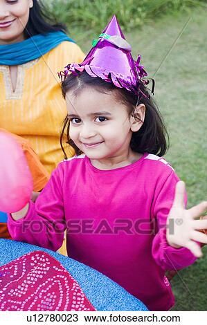Stock Image - Portrait of a girl playing with a balloon and her mother sitting beside her. Fotosearch