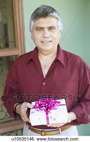 Stock Photograph - Portrait of a mature man holding a birthday present. Fotosearch