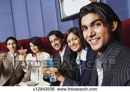 Stock Photograph - Portrait of two businesswomen and three businessmen sitting on a couch and holding glasses. Fotosearch