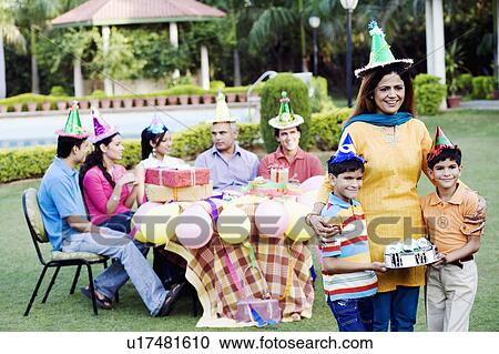 Stock Image - Two boys holding a birthday cake and standing with their mother. Fotosearch