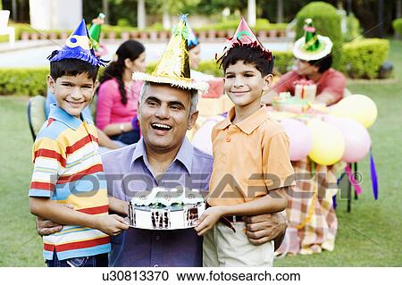 Stock Image - Two boys standing with their father and holding a birthday cake. Fotosearch