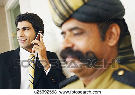 Businessman talking on a mobile phone behind a security guard View Large Photo Image Stock Photo - Businessman talking on a mobile phone behind a security guard. Fotosearch