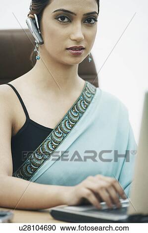 Stock Image - Businesswoman working on a laptop wearing a hands free device. Fotosearch