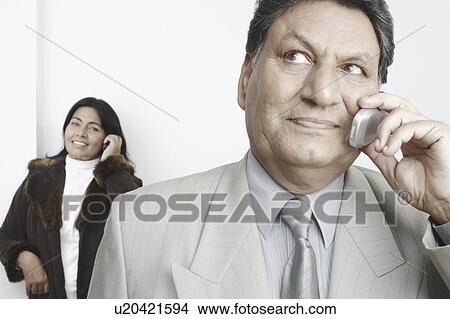 Close-up of a businessman talking on a mobile phone with a businesswoman standing behind him View Large Photo Image Picture - Close-up of a businessman talking on a mobile phone with a businesswoman standing behind him. Fotosearch