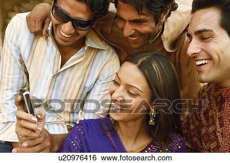 Stock Photograph - Close-up of three young men and a young woman looking at a mobile phone and smiling, Agra, Uttar Pradesh, India. Fotosearch