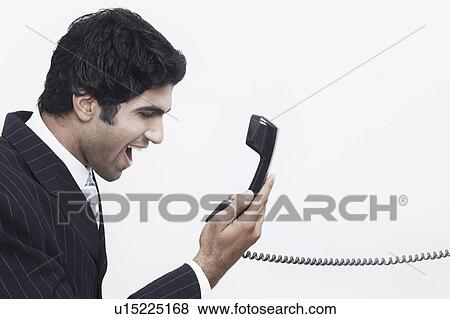 Stock Photo - Side profile of a businessman holding a telephone receiver. Fotosearch