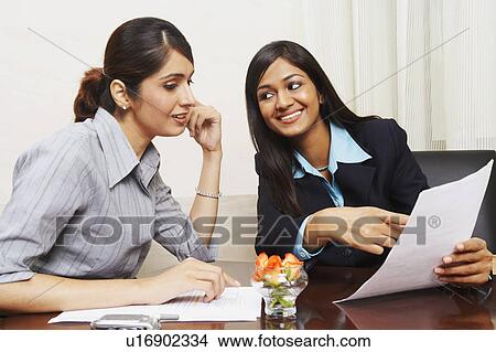 Picture - Two businesswomen sitting in an office and discussing documents. Fotosearch