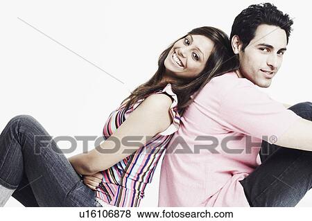 Stock Photo - Portrait of a young couple sitting back to back on the floor and smiling. Fotosearch