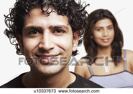 Stock Image - Portrait of a young man smiling with a young woman in the background. Fotosearch