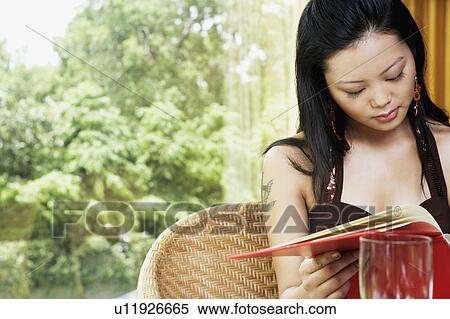 Stock Photography - Close-up of a young woman reading a menu card in a restaurant. Fotosearch