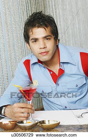 Portrait of a young man sitting in a restaurant and holding a martini glass View Large Photo Image Stock Photo - Portrait of a young man sitting in a restaurant and holding a martini glass. Fotosearch