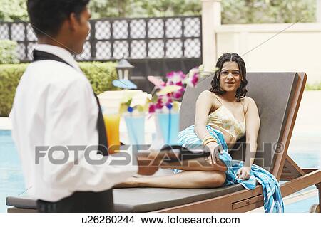 Portrait of a young woman reclining on a lounge chair with a waiter standing in front of her View Large Photo Image Picture - Portrait of a young woman reclining on a lounge chair with a waiter standing in front of her. Fotosearch