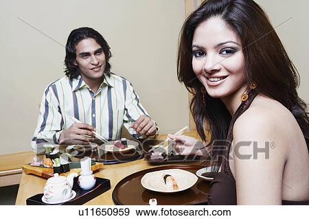 Stock Photo - Portrait of a young woman sitting with a young man at the dining table and smiling. Fotosearch