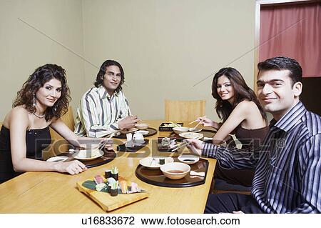 Stock Image - Portrait of two young couples sitting at the dining table and smiling. Fotosearch
