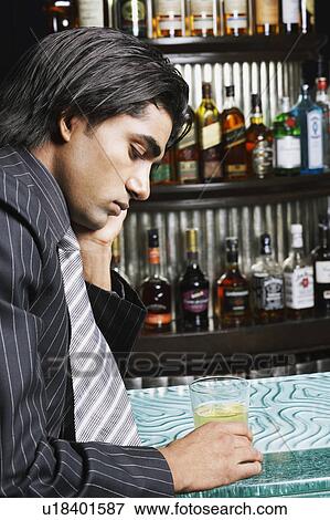 Stock Photo - Side profile of a businessman holding a glass of whiskey at a bar counter. Fotosearch