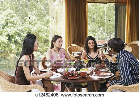 Stock Photograph - Three young women and a young man dining in a restaurant. Fotosearch