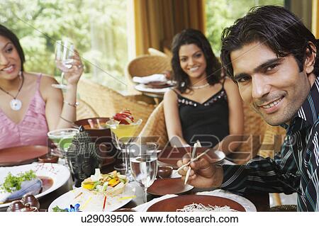 Stock Photograph - Two young women and a young man dining in a restaurant. Fotosearch