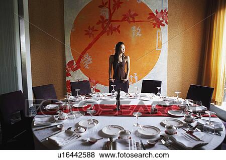 Stock Photo - Young woman standing behind a table in a restaurant. Fotosearch