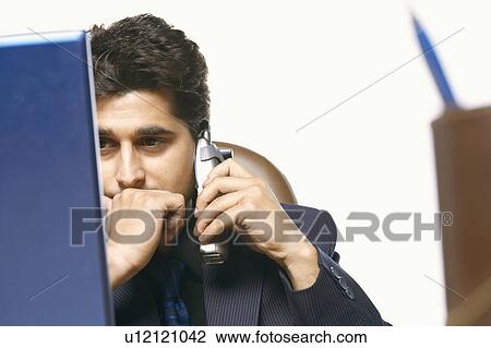 Stock Image - Close-up of a businessman talking on a cordless phone in front of a laptop. Fotosearch