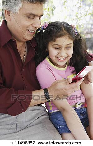Stock Image - Close-up of a mature man and his grandchildren looking at a mobile phone. Fotosearch