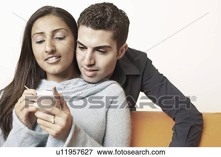 Stock Photo - Close-up of a young man behind a young woman using a mobile phone. Fotosearch