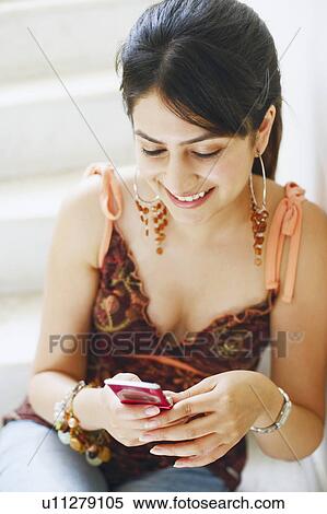 Stock Photography - Close-up of a young woman looking at a mobile phone and smiling. Fotosearch