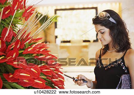 Close-up of a young woman standing near a plant and looking at a mobile phone View Large Photo Image Stock Image - Close-up of a young woman standing near a plant and looking at a mobile phone. Fotosearch