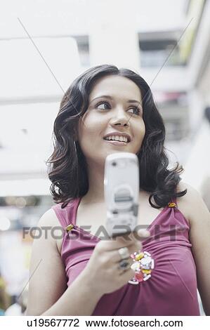 Low angle view of a young woman holding a mobile phone View Large Photo Image Stock Image - Low angle view of a young woman holding a mobile phone. Fotosearch