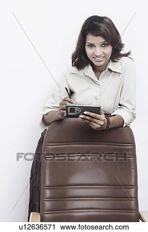 Portrait of a businesswoman leaning on a chair holding a mobile phone View Large Photo Image Stock Image - Portrait of a businesswoman leaning on a chair holding a mobile phone. Fotosearch