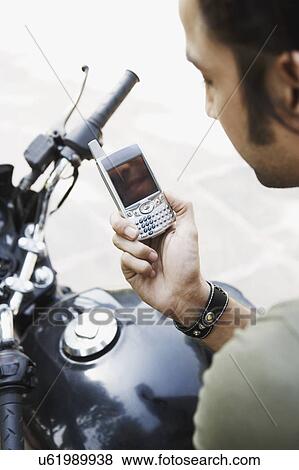 Side profile of a young man sitting on a motorcycle and using a mobile phone View Large Photo Image Stock Photo - Side profile of a young man sitting on a motorcycle and using a mobile phone. Fotosearch