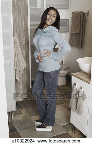 Portrait of a young woman standing on a weighing scale View Large Photo Image Picture - Portrait of a young woman standing on a weighing scale. Fotosearch