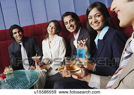 Stock Photo - Two businesswomen and three businessmen sitting on a couch and holding glasses. Fotosearch