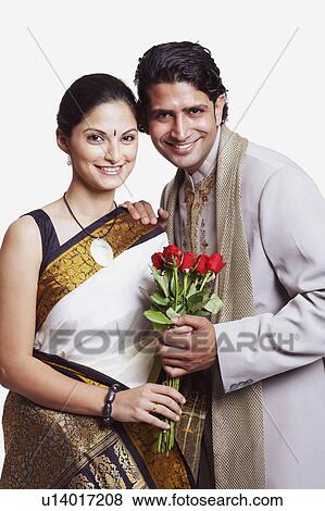 Stock Photo - Portrait of a young couple standing and holding a bunch of flowers. Fotosearch