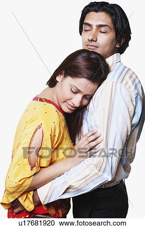 Stock Image - Side profile of a young couple embracing each other. Fotosearch