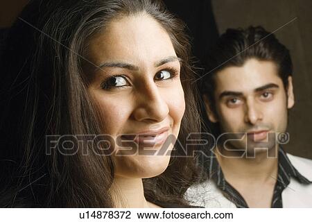 Stock Image - Portrait of a young woman grinning with a young man in the background. Fotosearch