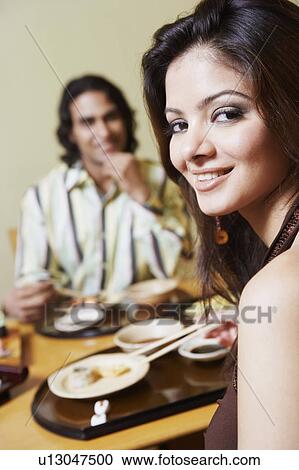 Stock Image - Portrait of a young woman sitting with a young man at the dining table and smiling. Fotosearch